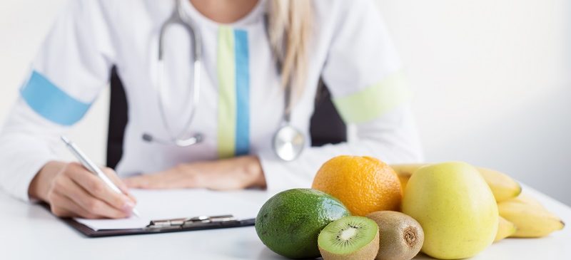 Une nutritionniste écrit la prescription destinée à une alimentation saine sur un bureau avec des fruits