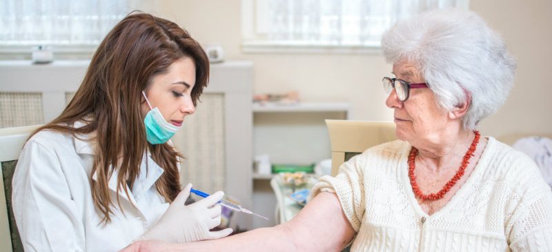 Une femme effectue une vaccination contre la grippe chez une femme âgée.