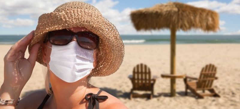 Femme qui porte son masque à la plage, avec chapeau, lunettes de soleil