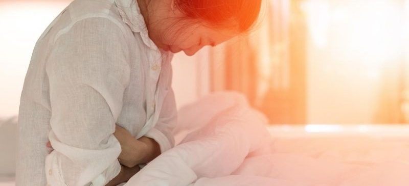 Femme assise dans son lit qui a mal au ventre