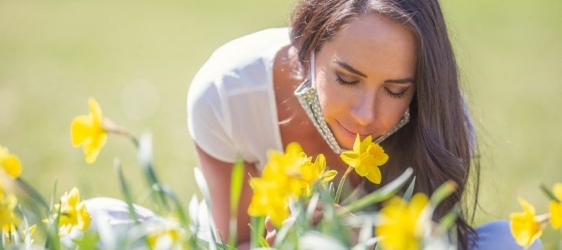 Femme qui sent l'odeurs des fleur, portant son masque en tissus sous le menton