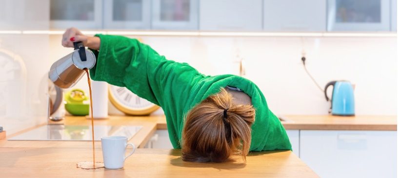 femme avec la tête contre le plan de travail se servant du café a coté de sa tasse