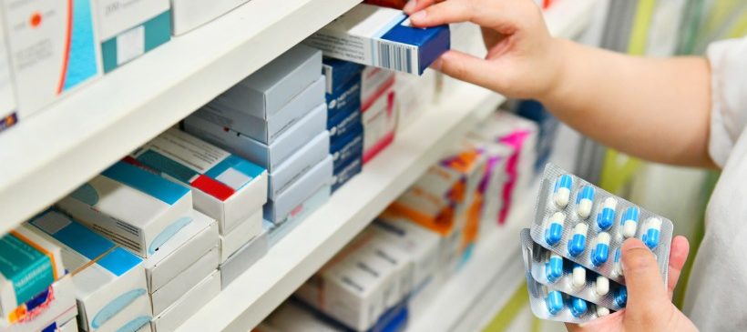 une main prenant une boite de médicaments dans un placard de pharmacie